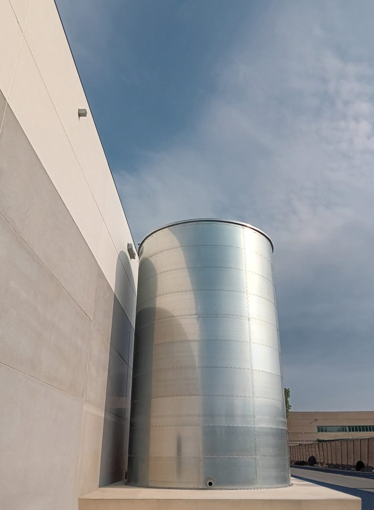 Serbatoio verticale in acciaio tra due pareti industriali.